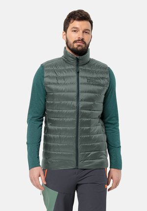 Groene gewatteerde vest met hoge kraag, rits aan de voorkant en merklogo. Draagt over een teal shirt met lange mouwen. Soepele textuur met een gewatteerd patroon.