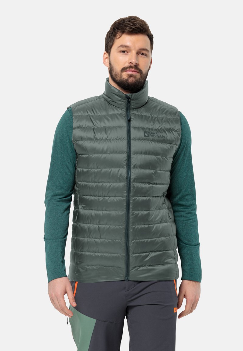 Gilet imbottito verde con colletto alto, zip frontale e logo del marchio. Indossato sopra una camicia a maniche lunghe color teal. Tessuto liscio con motivo trapuntato.