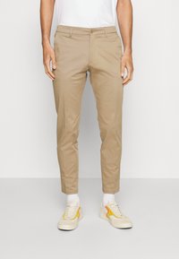 Beige bomullschinos med rak passform, med knappstängning och bältesöglor, i kombination med vita sneakers och ribbade vita strumpor.