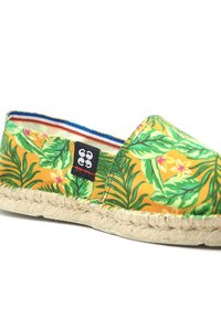 Espadrille jaune avec un imprimé tropical de feuilles et de fleurs, semelle en jute tissée et étiquette logo noire cousue sur la couture latérale.