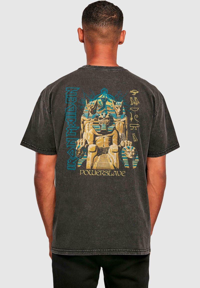 Melnā īsām piedurkņu T-kreklā ar krāsainu Egiptes motīvu druku un tekstu "Iron Maiden Powerslave" uz muguras.