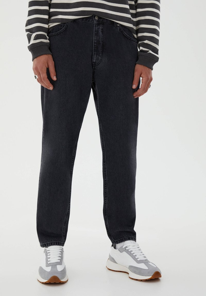 Jeans de mezclilla de lavado oscuro con un corte recto, que presentan un estilo clásico de cinco bolsillos y detalles de costura sutiles. Combinados con zapatillas grises y blancas.