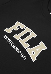 Czarna tkanina z dużymi beżowymi literami "FILA" obramowanymi na biało oraz mniejszym białym napisem "ESTABLISHED 1911" poniżej logo.