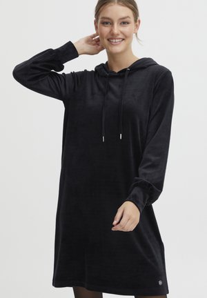 Schwarzes Kapuzenkleid aus weichem, samtigem Stoff. Hat lange Ärmel und einen lässigen Schnitt, mit Kordelzügen und einem kleinen Logodetail am Saum.