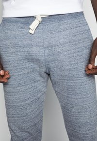 Los pantalones de chándal grises presentan una tela texturizada con un patrón sutil, una cintura elástica y un detalle de cordón atado.