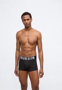 Μαύρα βαμβακερά μποξεράκια με λευκή ελαστική ζώνη που φέρει το λογότυπο "CALVIN KLEIN". Λείος υφή και στενή εφαρμογή.