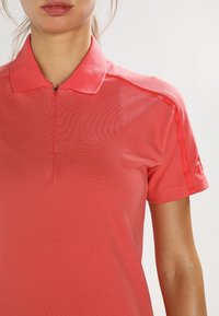 Korala koszulka polo z zamkiem, krótki rękaw, teksturowana tkanina i dyskretne logo na rękawie.