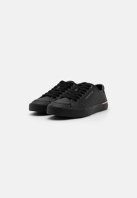 Zapatillas negras con material sintético suave, punta redonda, diseño con cordones y una franja en contraste en el lateral. Suela de goma texturizada.