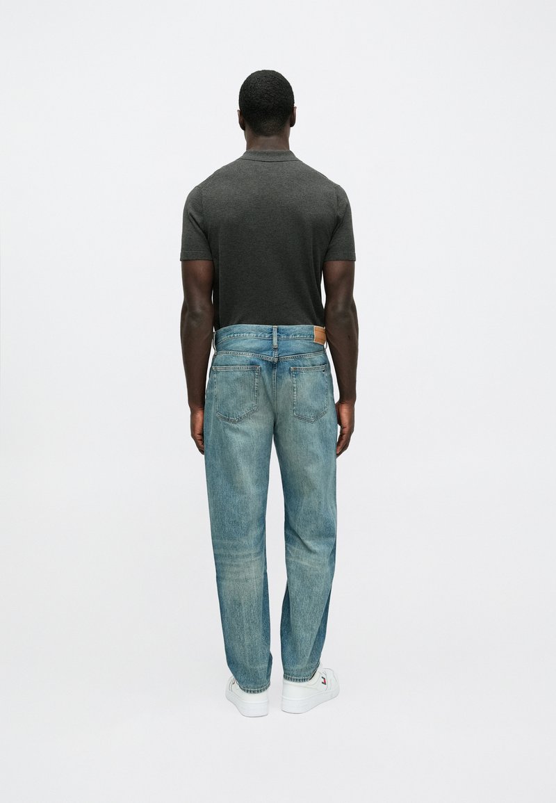 Dark gray short-sleeve t-shirt paired with light blue relaxed-fit denim jeans, featuring a contrasting brown leather patch at the waistband.