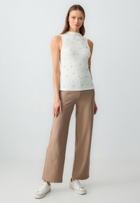 Top bianco senza maniche a coste con decorazioni testurizzate, abbinato a pantaloni a gamba larga beiges a righe e sneakers bianche.