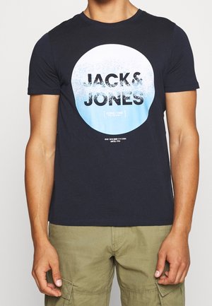 Man wearing black short-sleeve T-shirt with large white and blue circle graphic and "JACK & JONES" text, paired with olive cargo pants.