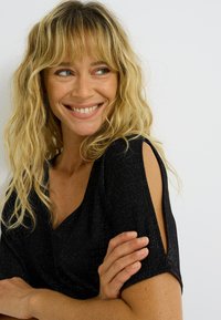 Haut noir avec un décolleté en V, manches courtes mettant en valeur des découpes. Texture scintillante, tissu doux et silhouette ajustée qui rehaussent son design.