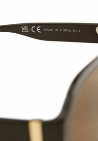 Détail de la branche des lunettes de soleil montrant les marques de certification UKCA et CE avec le texte « Made in China FC 3 » sur une monture noire.