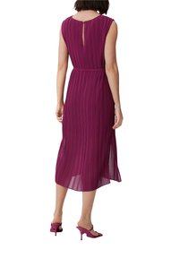 Plissiertes Midikleid in tiefem Magenta mit einem Rückenschlitz und einer taillierten Passform. Getragen mit passenden High Heels.