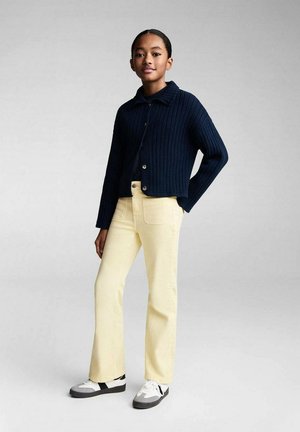 Navy ribbed cropped cardigan with button closure, paired with light yellow straight-leg jeans. Footwear features gray and white accents.