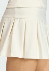 Biela plisovaná sukňa s textúrovanou tkaninou, vysokým pásom a rozšíreným dizajnom. Plisovanie pridáva hĺbku a pohyb k tomuto odevu.