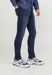 Blå denimjeans med slim fit, med fickor och en slät yta, matchade med marinblå och vita sneakers med meshdetaljer.