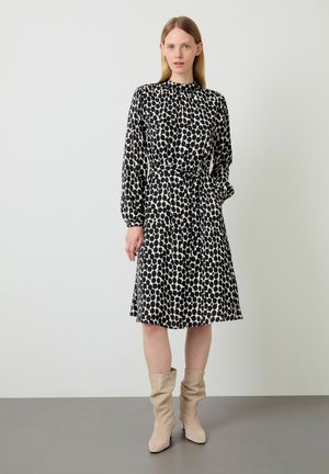 Robe noire et crème à pois avec des manches longues, un col froncé, une taille ceinturée et une jupe évasée. Associée à des bottes slouchy beige clair.