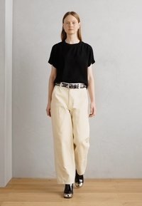 Haut noir à manches courtes associé à un pantalon large crème et une ceinture cloutée. Chaussures noires avec des accents métalliques brillants. Design simple et moderne.
