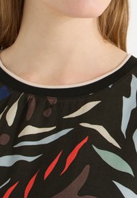 Gros plan d'un cou et d'une chemise à motifs multicolores avec un col côtelé noir et un léger liseré clair le long de l'encolure.