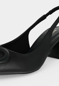 Μαύρο δερμάτινο παπούτσι με λουράκι στο πίσω μέρος, χαμηλό χοντρό τακούνι και μεγάλο κυκλικό διακοσμητικό στοιχείο στη μύτη.