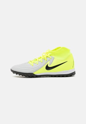 Le scarpe da calcio Nike Phantom presentano un corpo grigio, accenti giallo brillante, una superficie testurizzata e un logo nero. Progettate per il gioco su erba sintetica con suola ad alta trazione.