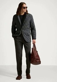 Σκοτεινό καπιτονέ μπουφάν με στενή εφαρμογή, γκρι παντελόνι και καφέ δερμάτινα παπούτσια. Κρατάει μια μεγάλη μπορντό τσάντα; τα γυαλιά ηλίου ολοκληρώνουν την εμφάνιση.