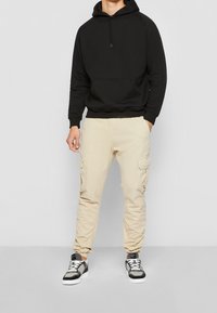 Svart huvtröja med framficka, kombinerad med ljusbeige cargobyxor med sidofickor. Svarta och vita sneakers fullbordar outfiten.