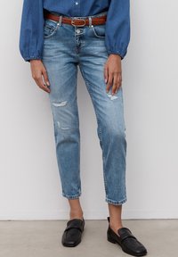 Vaqueros de mezclilla azul claro, con un corte relajado, detalles desgastados y dobladillos sin terminar. Combinados con mocasines negros.