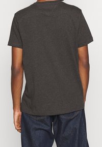 Šedé tričko s krátkým rukávem a kulatým výstřihem, vyrobené z měkké bavlny, zobrazené zezadu s volným střihem a minimálním švem.