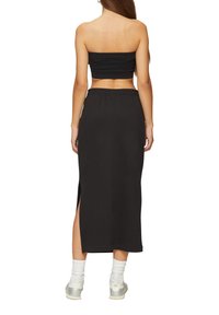 Zwarte off-the-shoulder crop top gecombineerd met een zwarte midi-rok met een zijsplit en een elastische tailleband. Draagt het met lichtgekleurde sneakers.