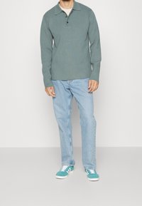 Polo vert clair à manches longues avec col, patte à trois boutons, associé à un jean droit bleu clair et des baskets turquoise.