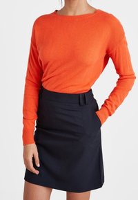 Pull en tricot à manches longues orange associé à une mini-jupe bleu marine foncé avec poches latérales et texture lisse.