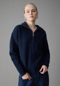 Maglione lavorato a maglia blu navy con colletto a zip a un quarto, texture a coste e dettaglio della zip in tono oro. Presenta maniche lunghe e una vestibilità comoda.