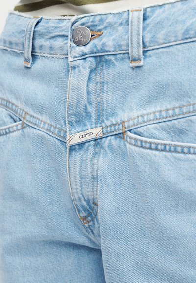 Φωτεινό γαλάζιο τζιν με ορατές μπροστινές τσέπες, μεταλλικό κουμπί με την επιγραφή «CLOSED» και μια μικρή λευκή ετικέτα με το κείμενο «CLOSED» στη λωρίδα κουμπώματος.