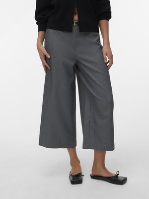 Frau trägt graue weite, verkürzte Hosen, schwarzen Taillengürtel, schwarzen Cardigan und schwarze Ballerinas mit quadratischer Spitze.