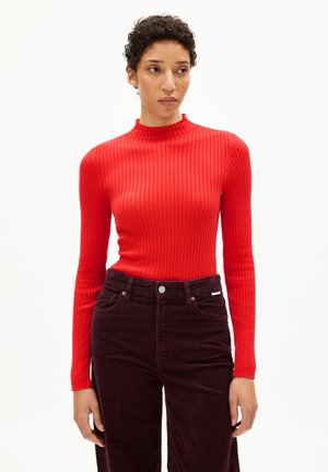 Rode geribbelde langemouwtop met een hoge halslijn, gecombineerd met donkerpaarse corduroy broek met voorzakken en een knoopsluiting.
