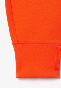 Orange sweatshirtmanschett med ribbad textur. Har en märkeslapp i matchande färg, som framhäver sömlös sömnad och slät finish.