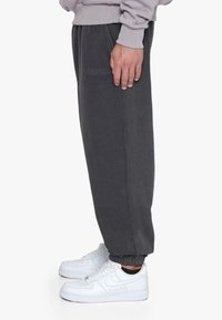 Grå joggingbukser med elastisk talje, ribbede manchetter og præget "DROPSIZE" logo langs siden, parret med hvide sneakers.