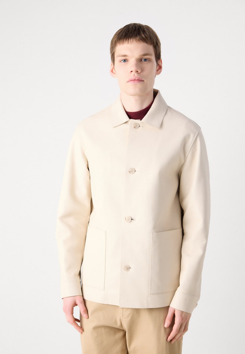Lichtbeige jack met een kraag, voorzien van drie knopen aan de voorkant, twee voorzakken en een gladde textuur. Gedragen over een bordeauxkleurig shirt.