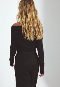 Zwarte off-the-shoulder blouse met lange mouwen, gecombineerd met hoge taillebroek in zwart. Zachte stof met een slim fit, met gedetailleerde mouwmanchetten.