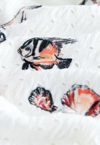 Tissu blanc avec un motif texturé présentant des poissons tropicaux imprimés en orange, noir et blanc, ainsi que des coquillages.