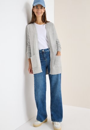 Grijze gebreide cardigan met zakken, gedragen over een witte t-shirt en blauwe wijde jeans, gecombineerd met witte sneakers en een lichtblauwe pet.