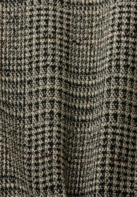 Texture de tissu pied-de-poule noir et blanc avec un motif de grille brun subtil, présentant de légers plis et un aspect tricoté.