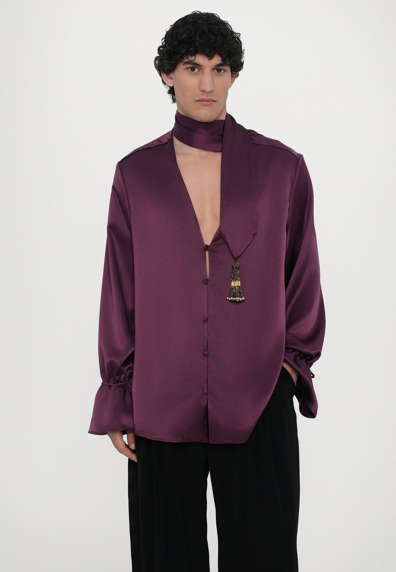 Purple satin shirt with a deep V neckline, button front, and wide sleeves featuring ruching at cuffs; includes a matching neck scarf with a decorative tassel.