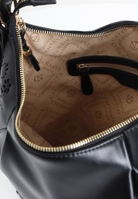 Borsa a tracolla in pelle nera con zip e dettagli in tonalità oro. L'interno presenta una fabbrica beige con un motivo logo ripetuto. Ha una tasca con zip.