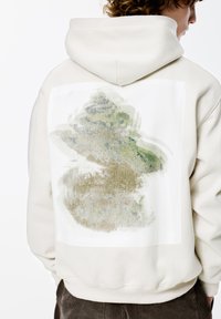 Lichtbeige hoodie met een gladde textuur, met een groot abstract groen en beige ontwerp op de achterkant binnen een wit rechthoekig paneel.