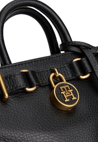 Poignée et bandoulière en cuir noir texturé avec anneau doré et cadenas rond arborant des initiales de logo gravées.