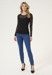 Zwarte lange mouw top met een gestructureerd gestreept patroon, in combinatie met strakke blauwe jeans en zwarte puntige hakken. Schoon, eenvoudig ontwerp.