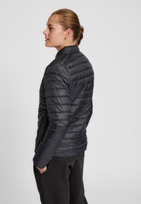 Giubbotto imbottito nero con cuciture orizzontali, colletto alto e tasche con cerniera. Texture liscia e design leggero per il calore.